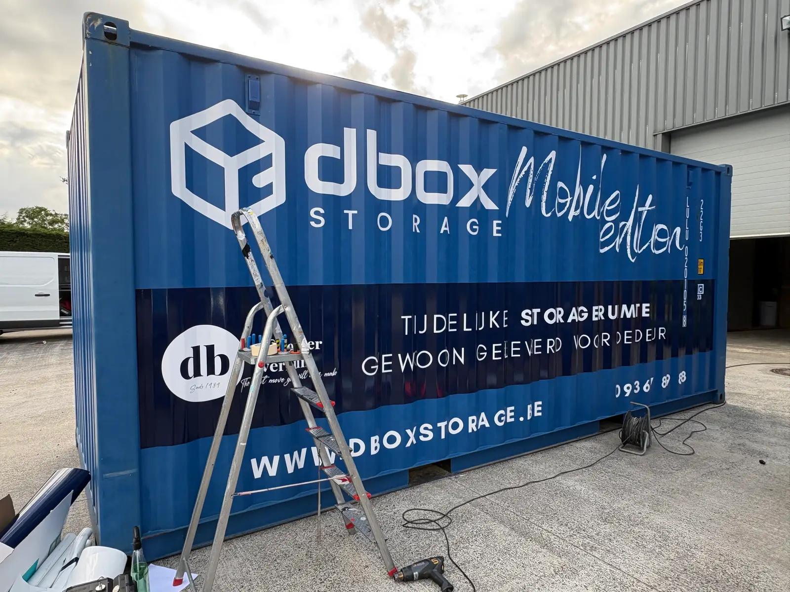 Opslagcontainer met grote witte belettering, montage met ladder op locatie