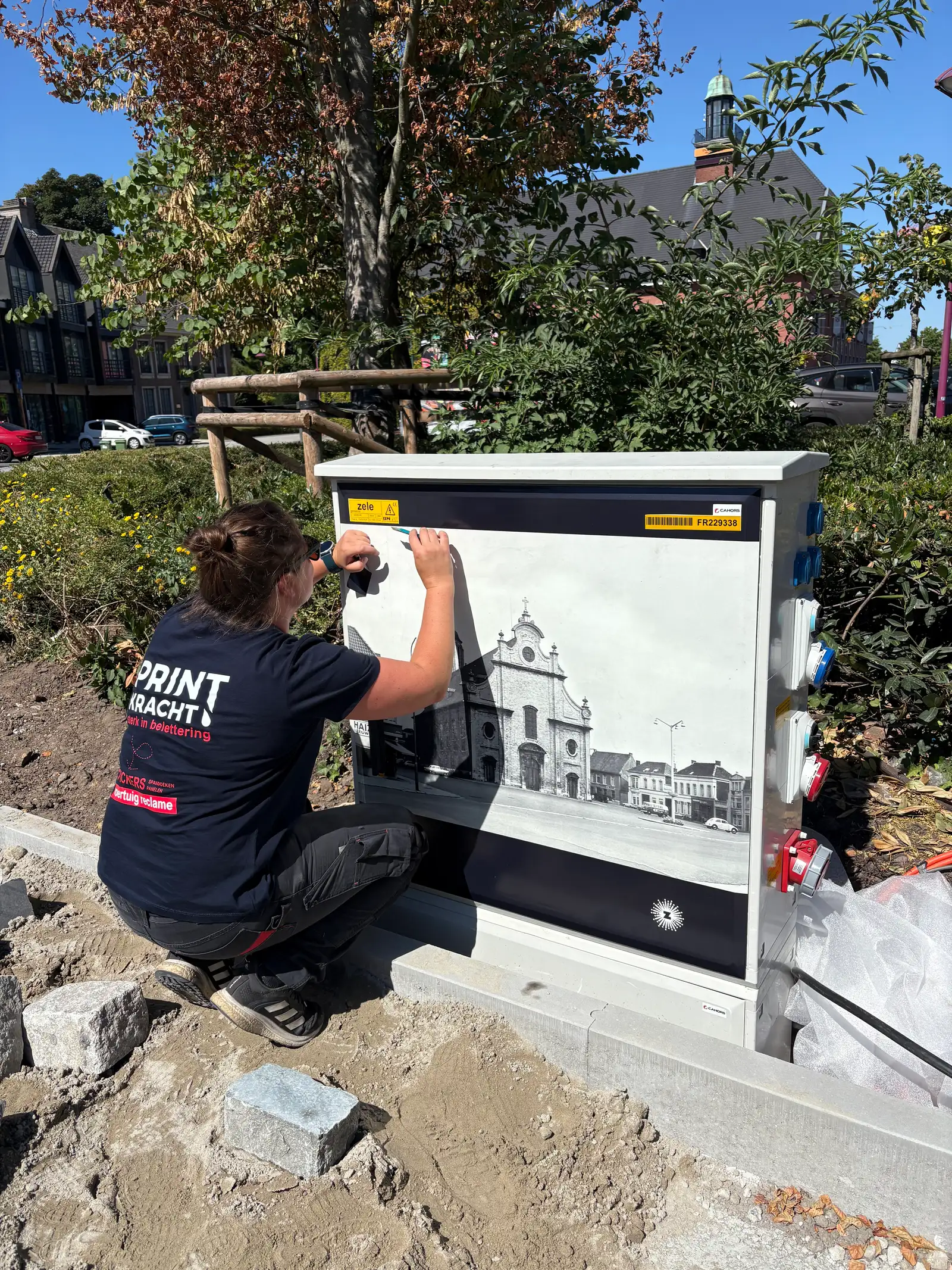 Printkracht-medewerker beplakt een elektriciteitskast met een fotoprint op locatie