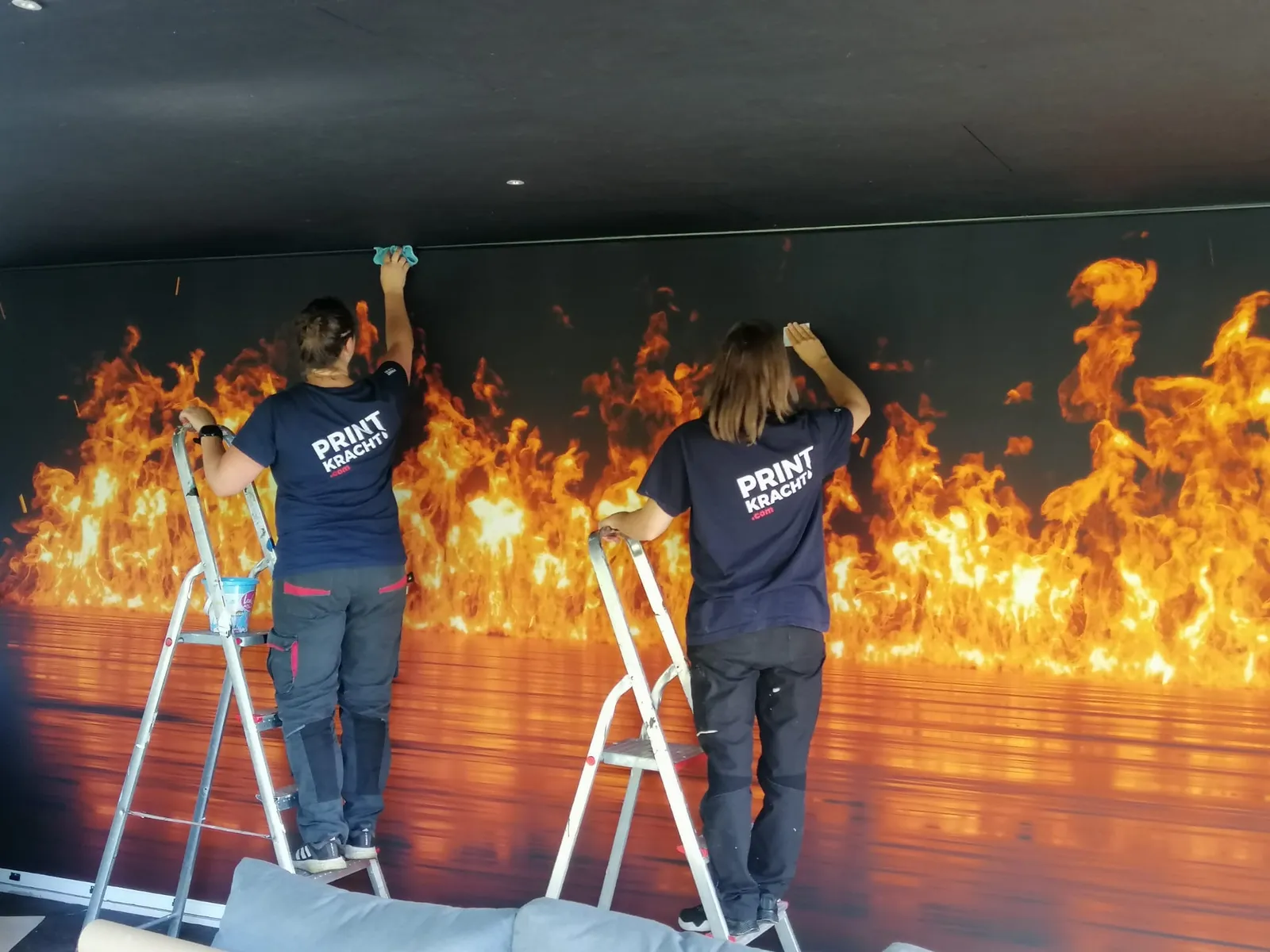 Montage van een groot textielframe met vlammen-print in een loungeruimte