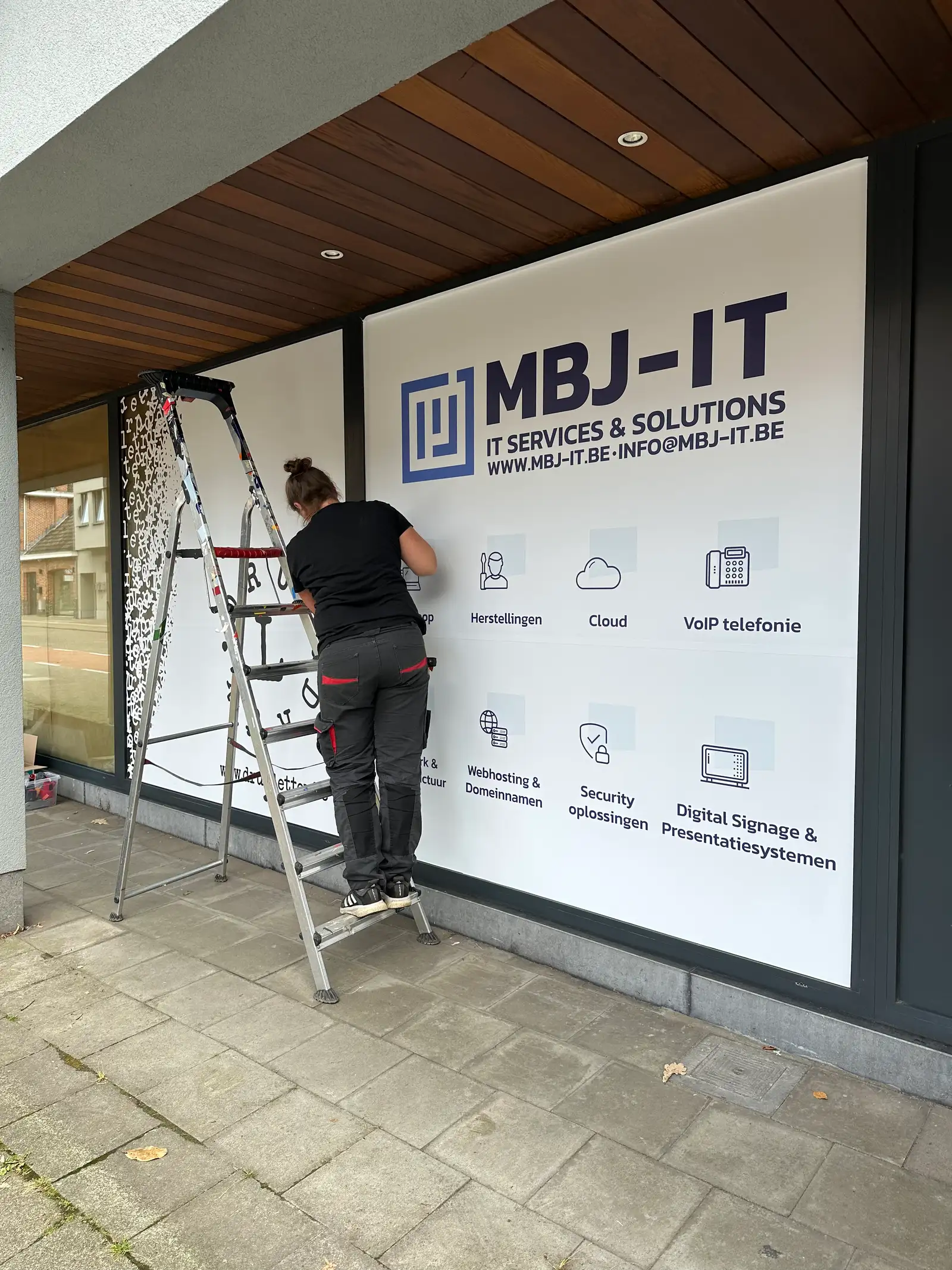 Medewerker plaatst fullcolor raambelettering op een kantoorvitrine