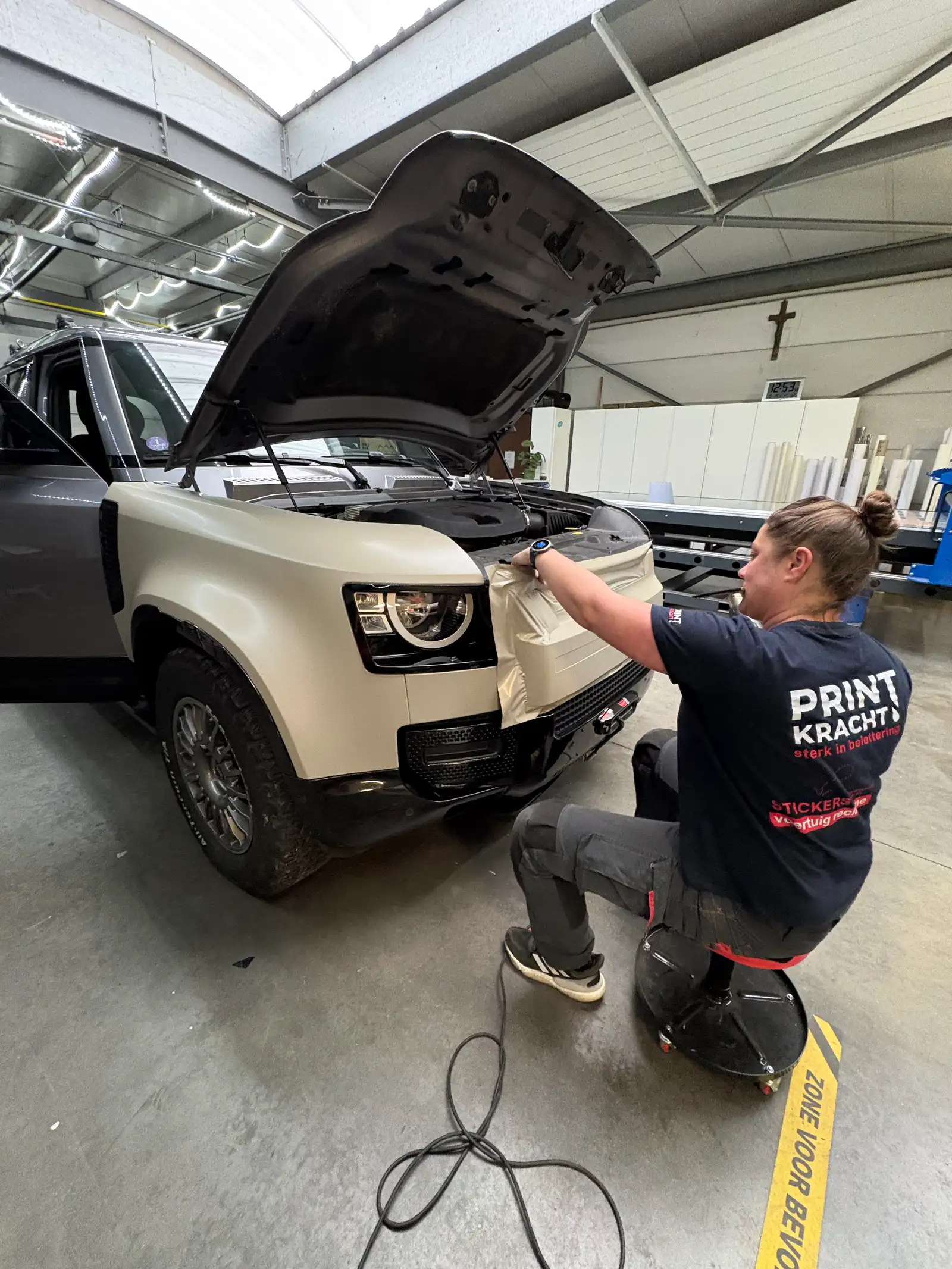 Medewerker brengt folie aan op de motorkap van een terreinwagen tijdens een full wrap in het atelier